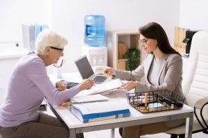 Pretty young female agent helping senior client to fill in insurance document