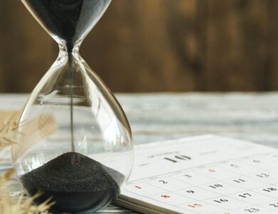 Hourglass with calendar on wooden desk close up