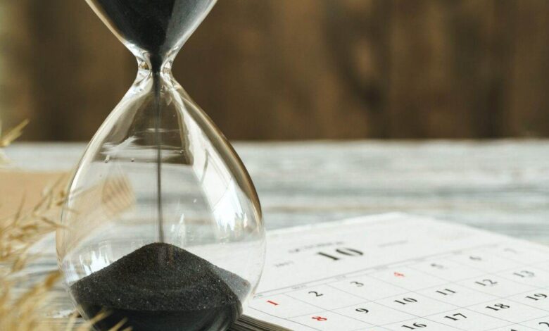 Hourglass with calendar on wooden desk close up