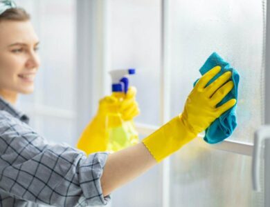 Young housekeeper washing window glass with rag and spray detergent, selective focus