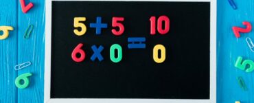 top view of blackboard with math sums, colorful numbers and paper clips on blue wooden background